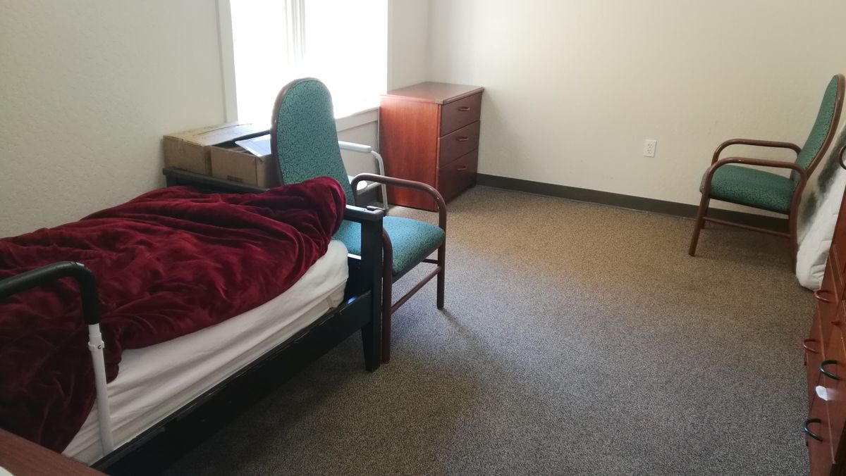 A minimalist bedroom with a bed, chair, and a window.