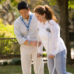 A person assisting another with crutches during a physical therapy session outdoors.