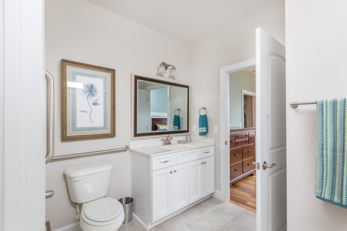 A modern bathroom with a white interior, featuring a sink with a mirror above, and a toilet beside decorative frames.