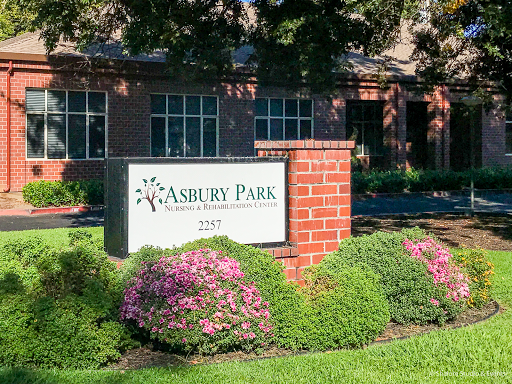 A welcoming entrance sign for Ashbury Park, surrounded by lush greenery and colorful flowers.