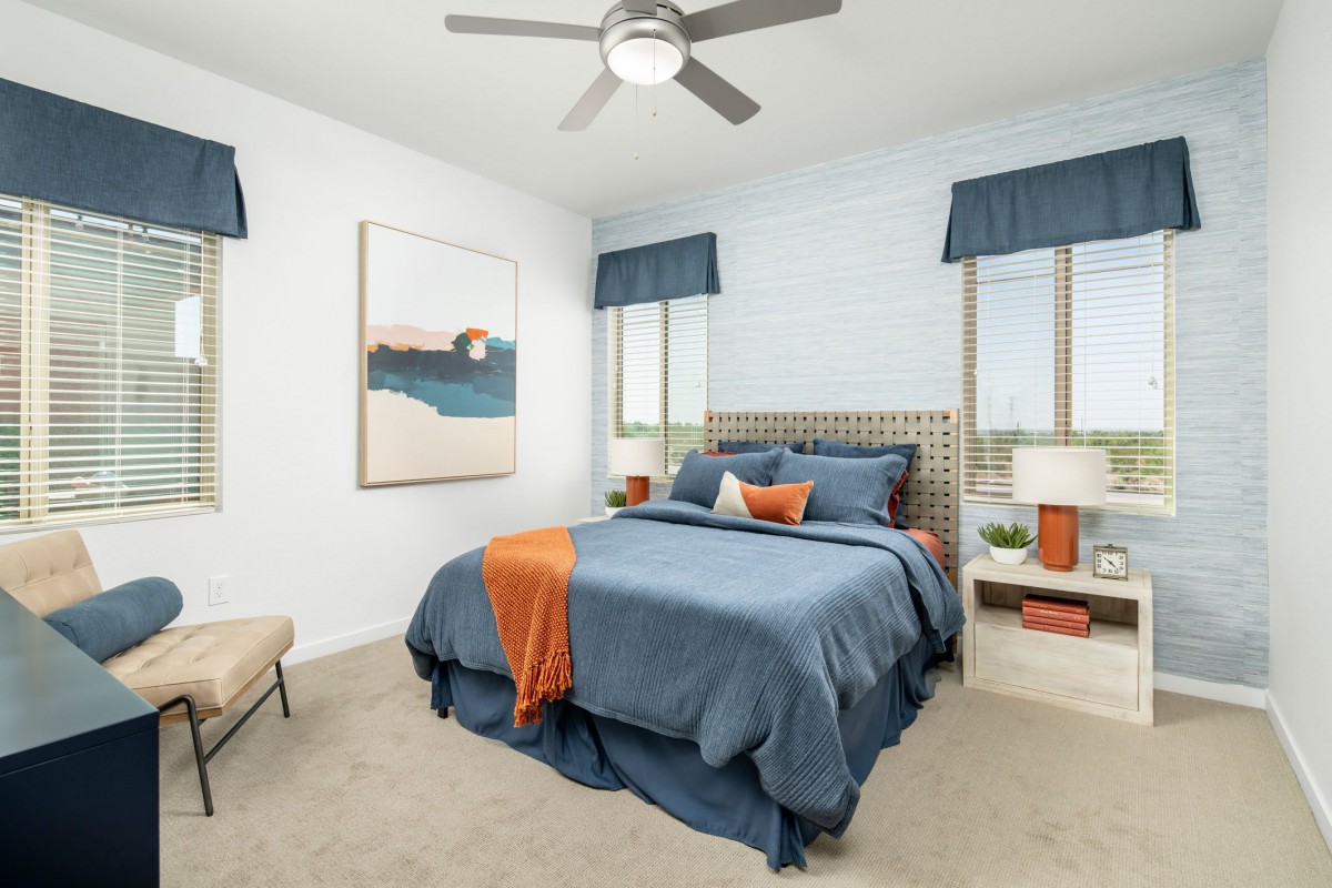 A modern bedroom with blue bedding and orange accents, featuring large windows and stylish decor.