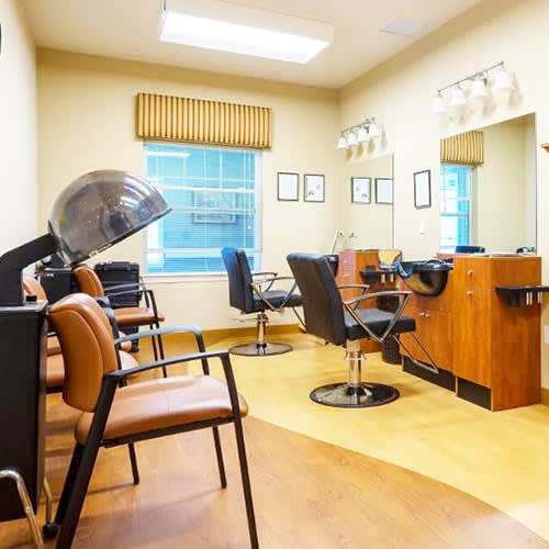 A well-lit hair salon interior with styling chairs, a hooded hair dryer, and mirrors.