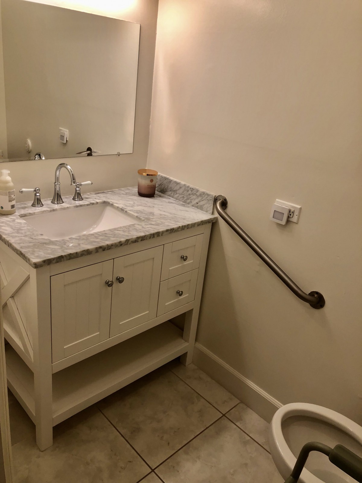 A bathroom with a sink and vanity, featuring a marble countertop and a grab bar.