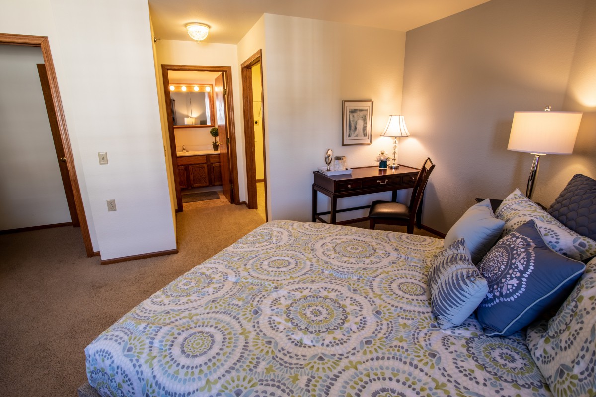 A cozy bedroom with a patterned bedspread, desk, and lamp.