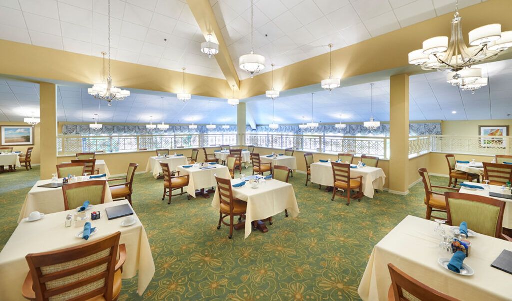 A spacious restaurant dining area with neatly arranged tables and chairs, large windows, and elegant lighting.