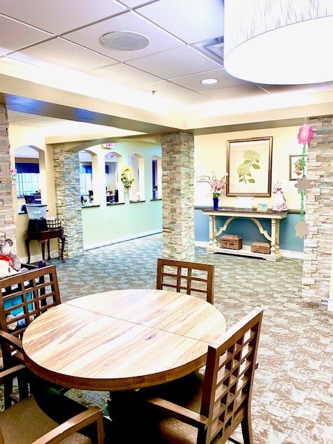 A cozy interior space with a round wooden table, chairs, and stone columns leading to a reception area.