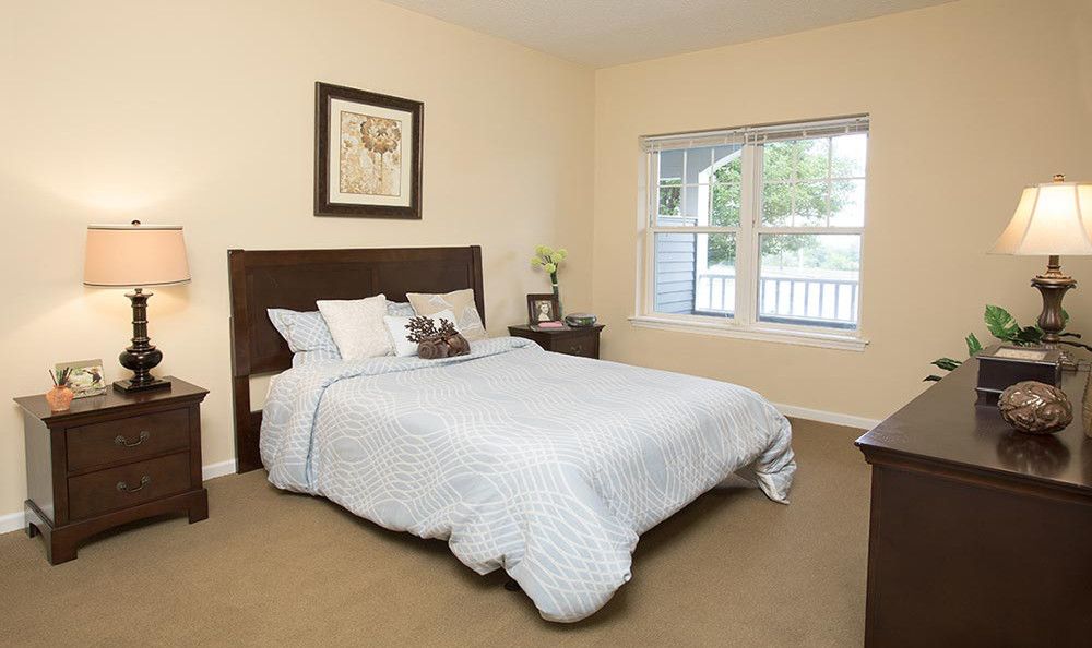 A cozy, well-lit bedroom featuring a neatly made bed with a large window allowing natural light.