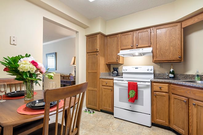 A cozy kitchen with wooden cabinets and a white stove, adjacent to a dining area.