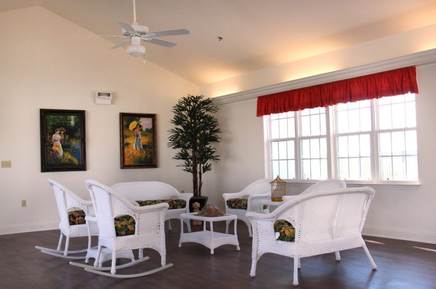 A cozy living room featuring white wicker furniture, decorative artwork, and ample natural light.