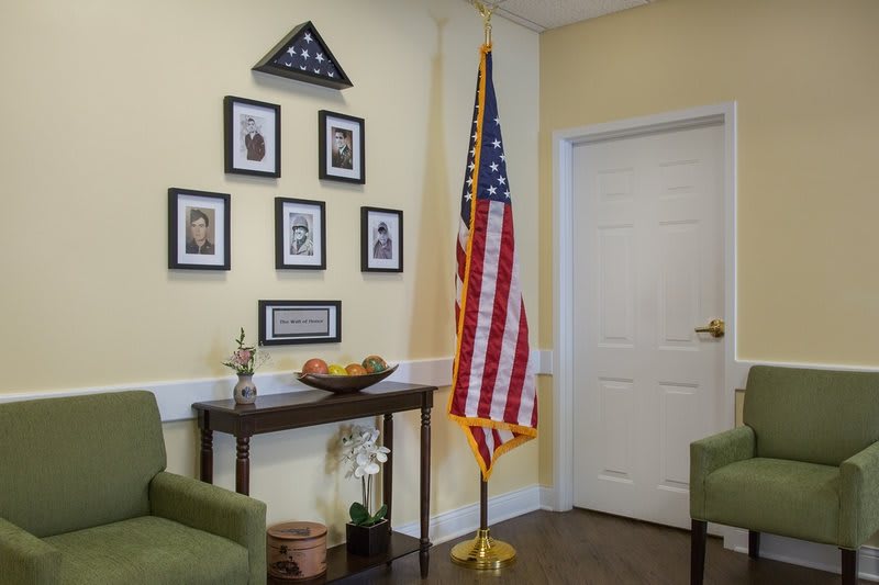A room decorated with an American flag, framed photos, and a small table against a light-colored wall.