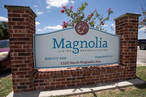 A welcoming sign for Magnolia Living Facility, surrounded by blooming flowers and a clear blue sky.