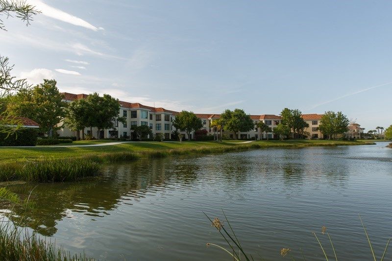 A serene residential apartment complex overlooking a calm lake and surrounded by greenery.
