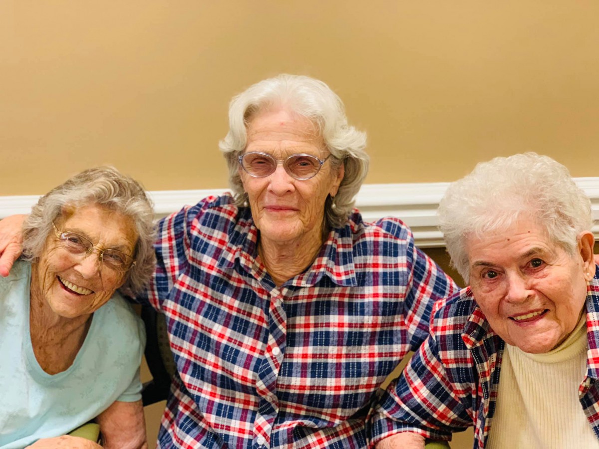 Three elderly women sitting together and smiling indoors.