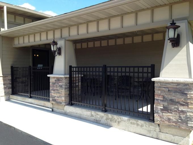A building exterior featuring a stone wall and a black metal fence enclosing a small patio area.