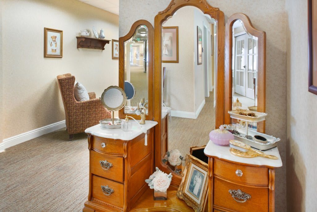An elegant wooden vanity table with a three-panel mirror in a cozy bedroom setting.