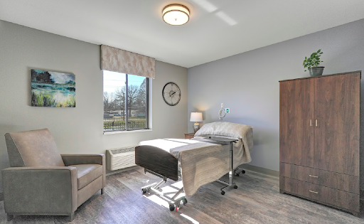 A modern hospital room featuring a patient bed, comfortable furniture, and natural light from the window.
