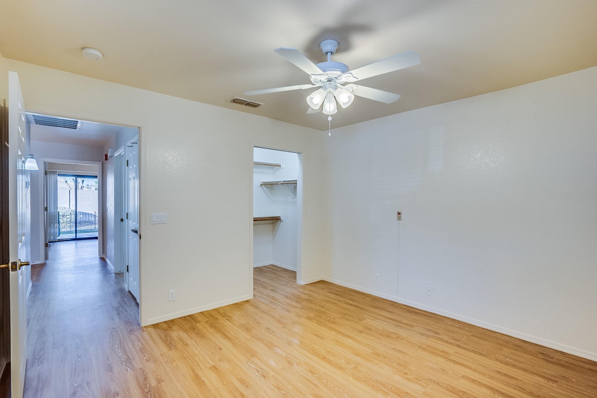 An empty room with wood flooring and a ceiling fan, featuring white walls and a visible doorway.