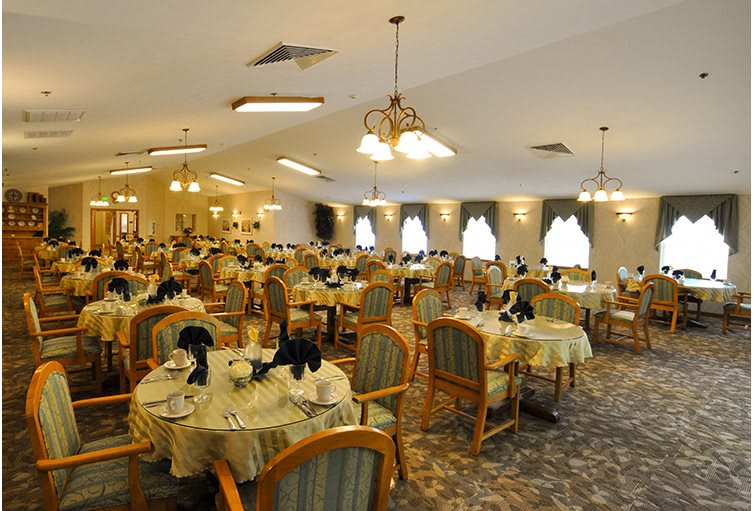 Elegantly set dining room with multiple tables and chairs, illuminated by warm lighting.