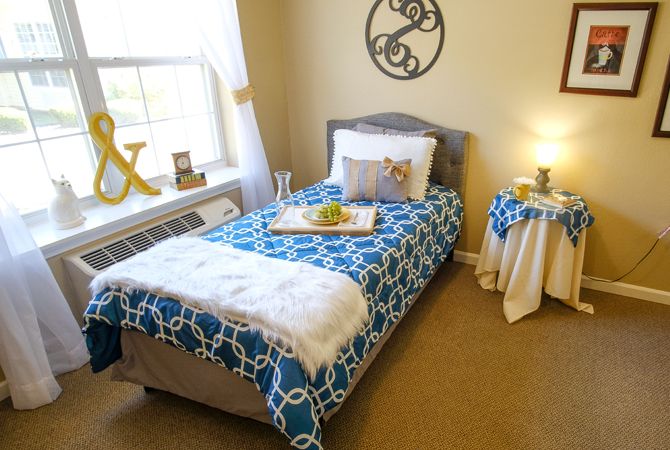 A cozy bedroom with a single bed adorned with a blue patterned blanket, complemented by soft lighting and decor.