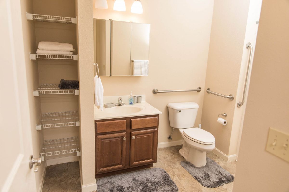 A clean and organized bathroom with a sink, toilet, mirror, and shelving unit with towels.