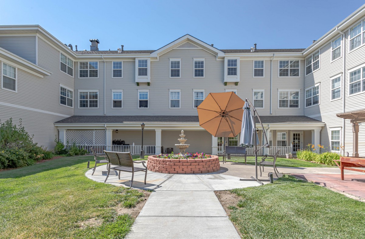 A sunny courtyard with outdoor seating and umbrellas in front of a multi-story residential building.