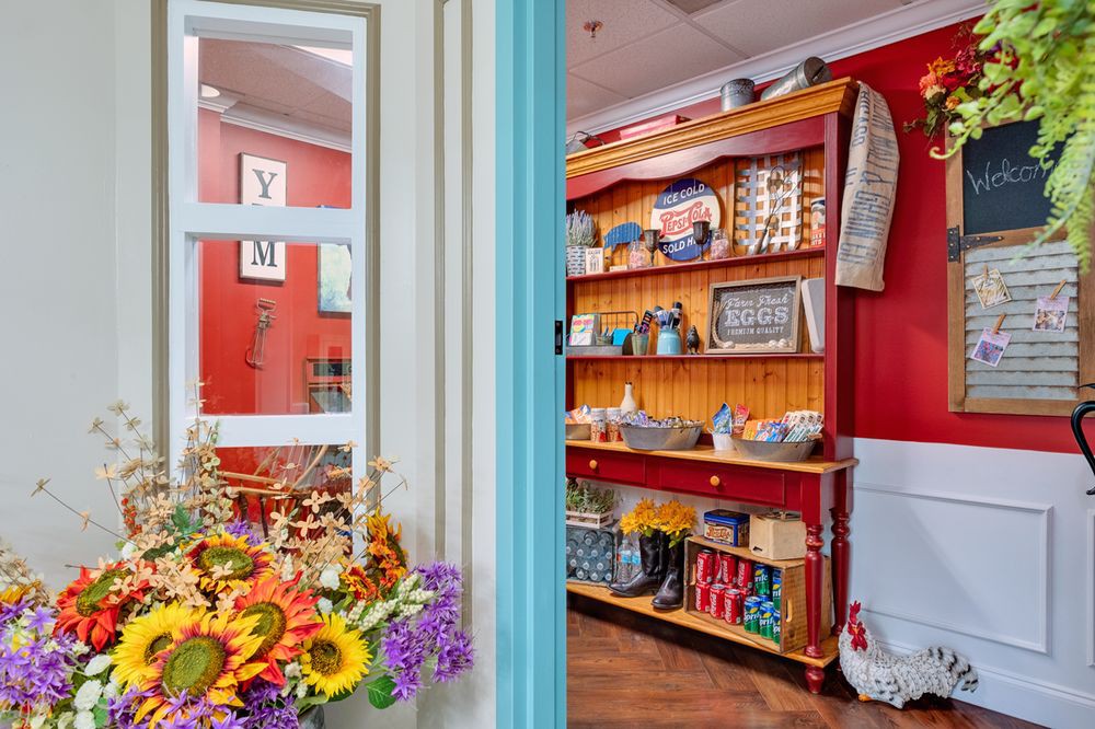 A cozy cafe interior with bright red walls, colorful flowers, and vintage-style shelves filled with various items.