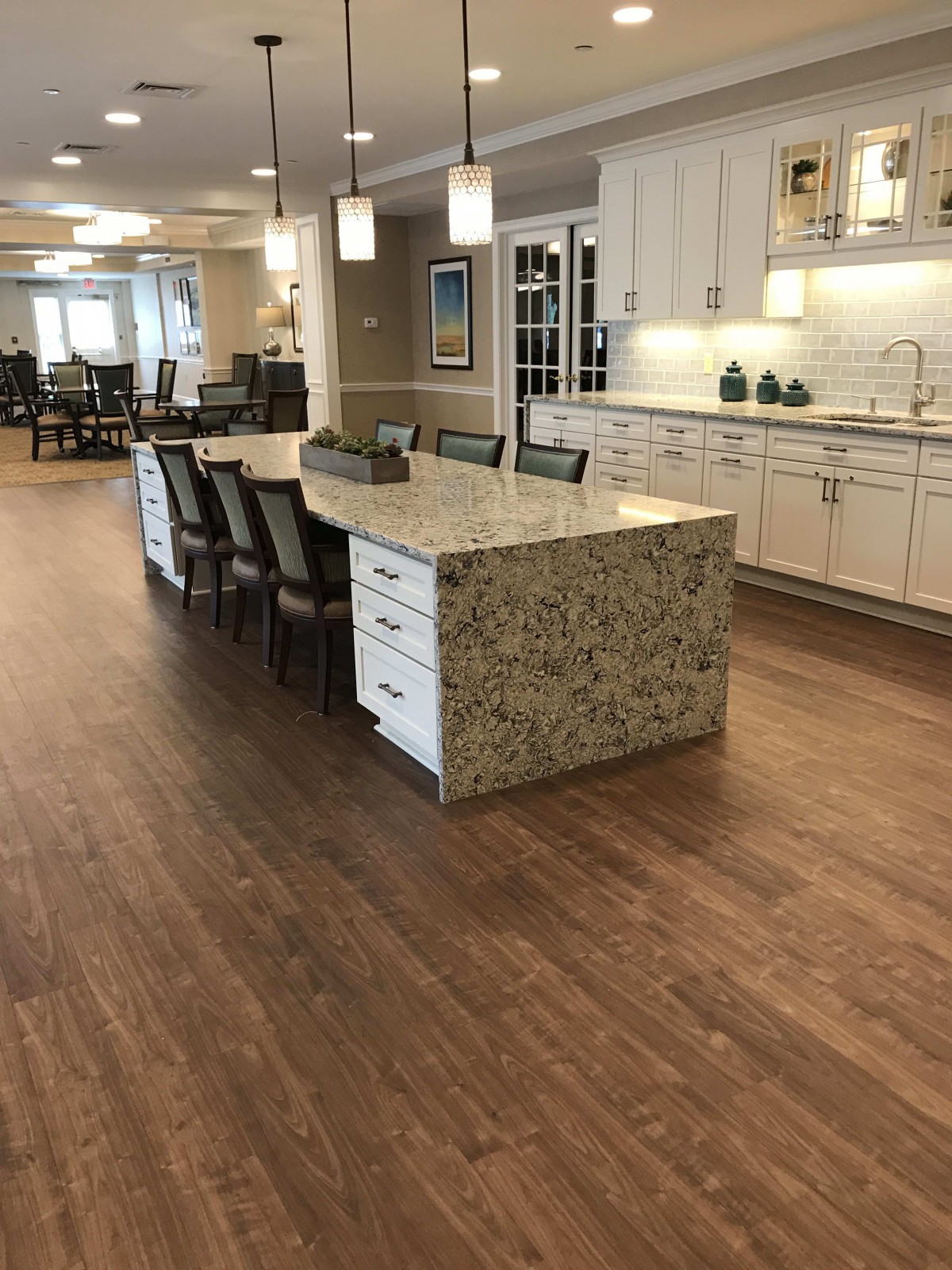 A modern kitchen with a large granite island and wooden flooring.