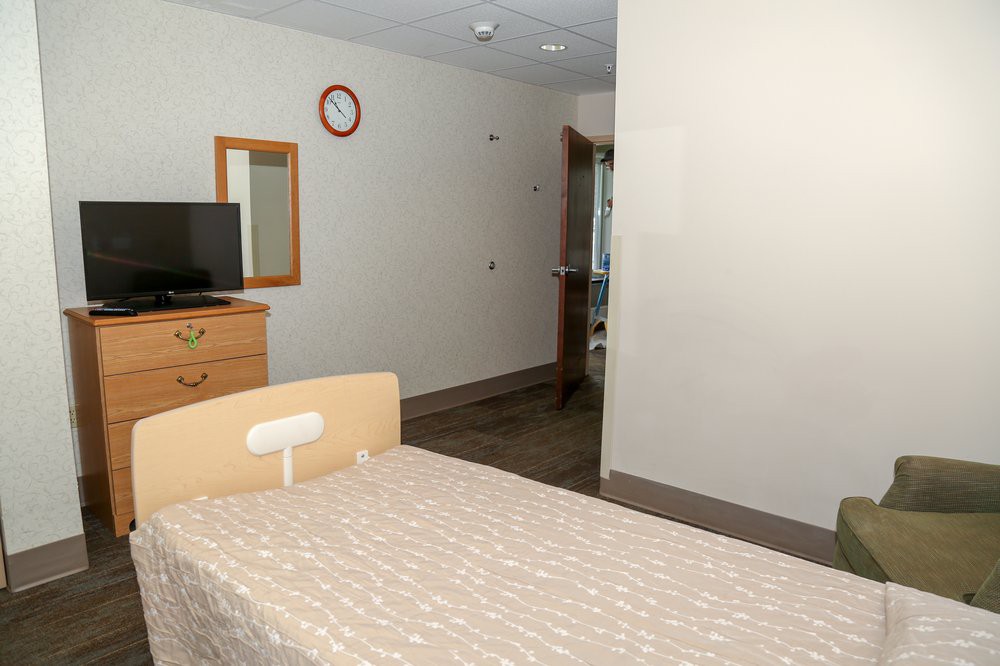 A clean hospital room with a bed, television, and simple furniture.