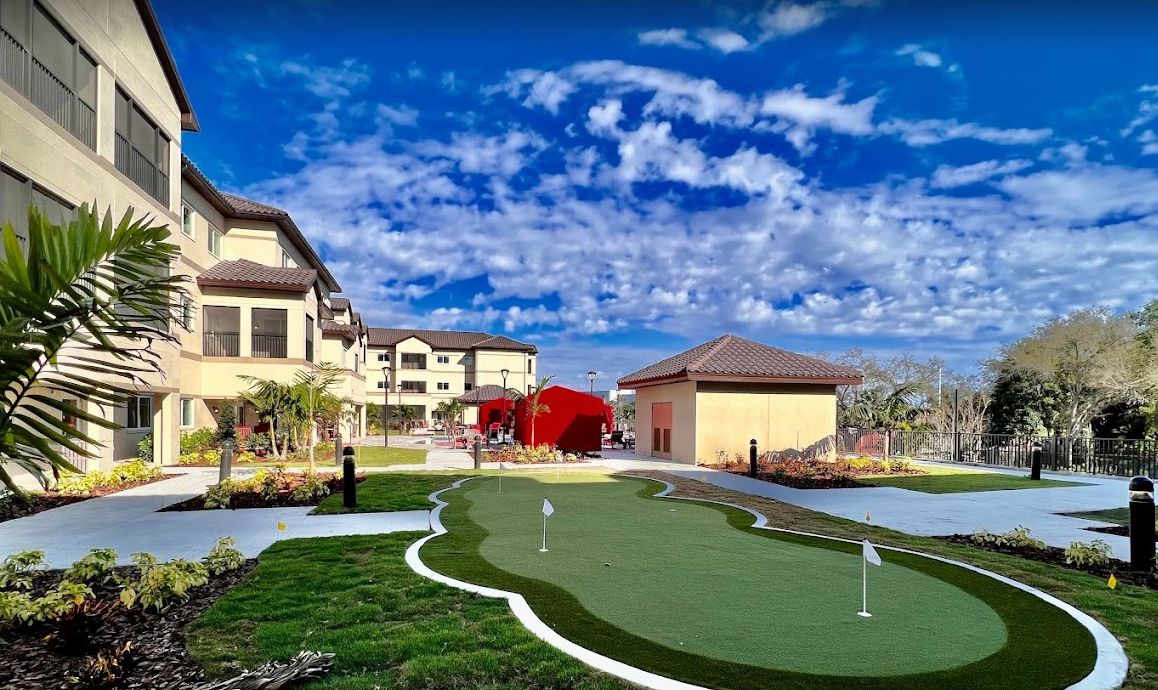 Scenic view of a putting green surrounded by buildings under a bright, cloudy sky.
