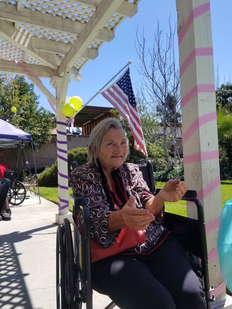 A woman in a wheelchair sits under a decorated pergola with an American flag in the background.