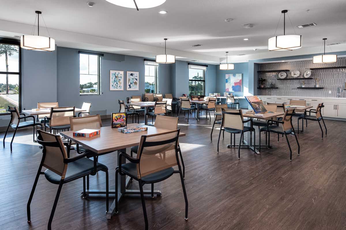 A modern dining area with neatly arranged tables and chairs, featuring soft lighting and a hardwood floor.