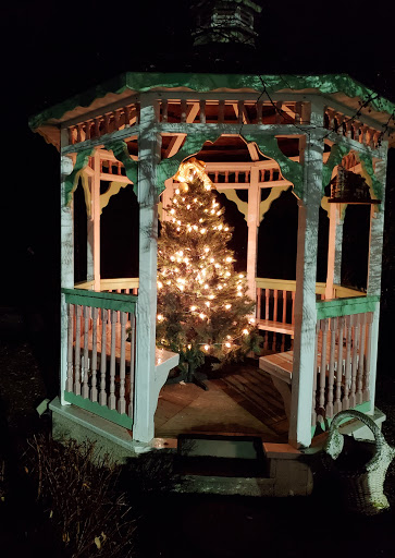 A beautifully decorated gazebo featuring a glowing Christmas tree, creating a festive atmosphere on a serene night.