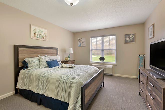 A cozy bedroom with a large bed, artwork on the walls, and a window letting in natural light.