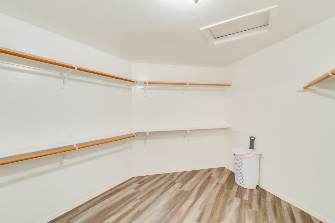 An empty walk-in closet with wooden floors and white shelves.