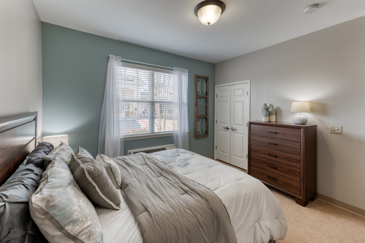 A cozy and modern bedroom featuring a neatly made bed, a dresser, and soft lighting with natural light streaming in through a window.