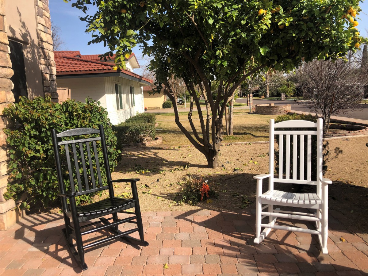 Two rocking chairs on a sunny patio with a view of a garden.