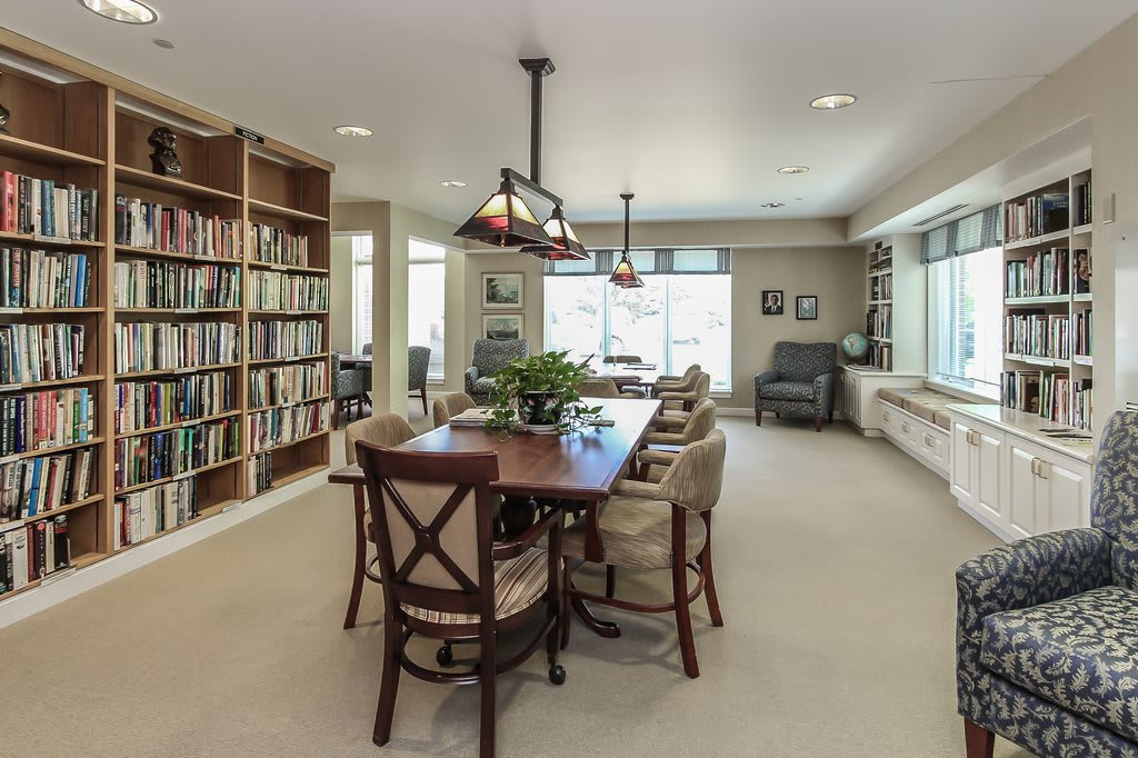 A cozy living room featuring a dining table, bookshelves, and ample natural light.