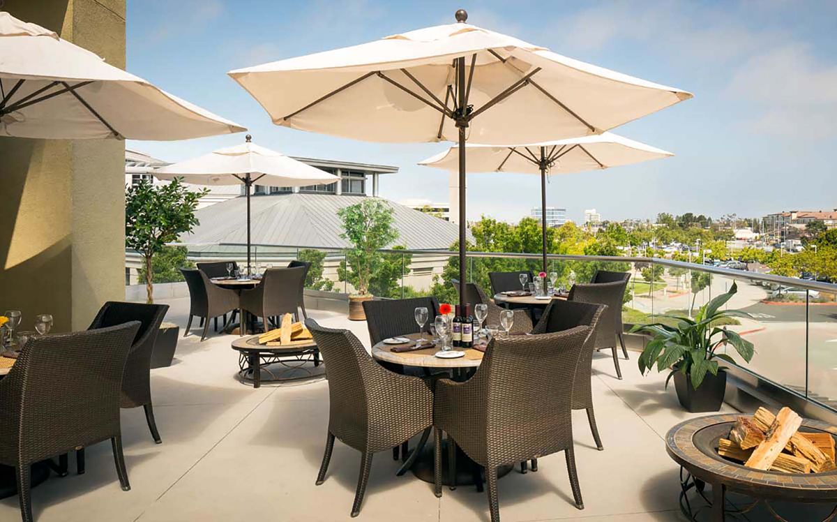 A sunny outdoor restaurant patio with tables, chairs, and umbrellas.