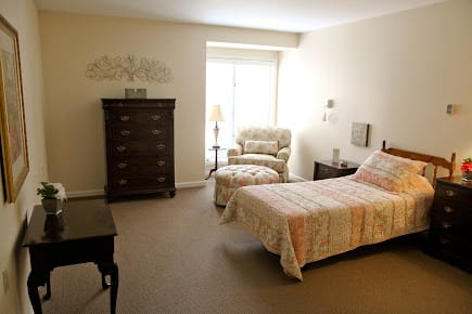 A cozy, well-furnished bedroom with a single bed, armchair, and dresser.