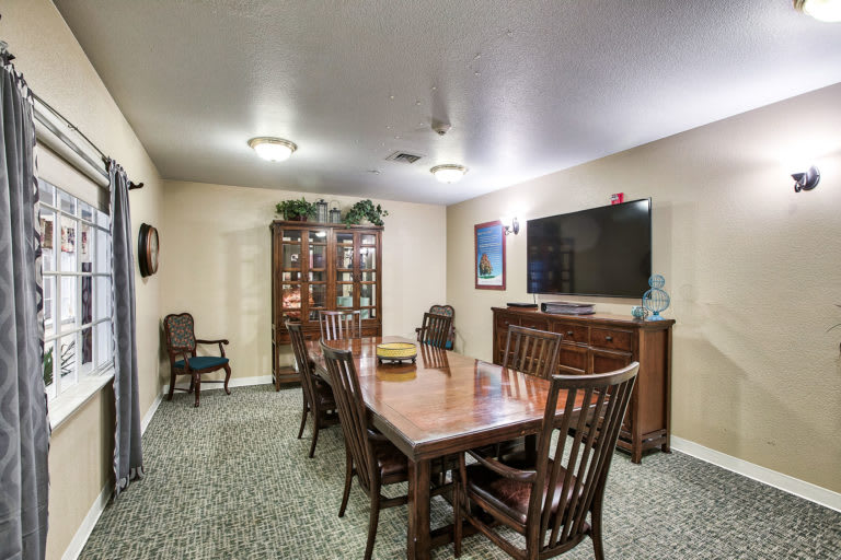 A well-furnished dining room with a large table, chairs, cabinet, and wall-mounted television.