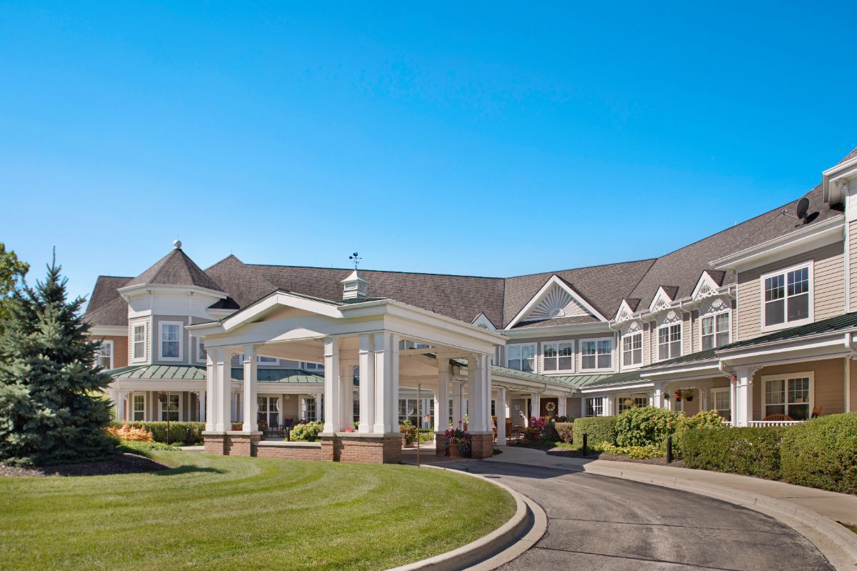 A large estate with a circular driveway and well-maintained landscaping under a clear blue sky.