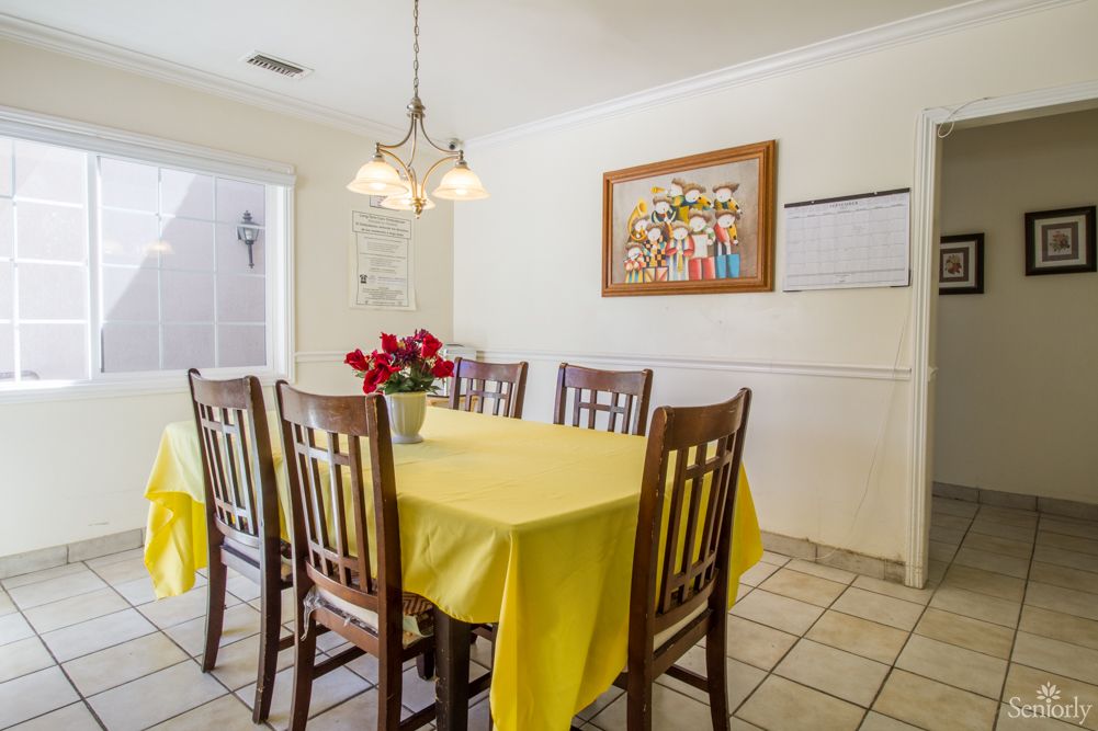 A dining room with a yellow tablecloth, surrounded by wooden chairs and decorated with flowers and wall art.