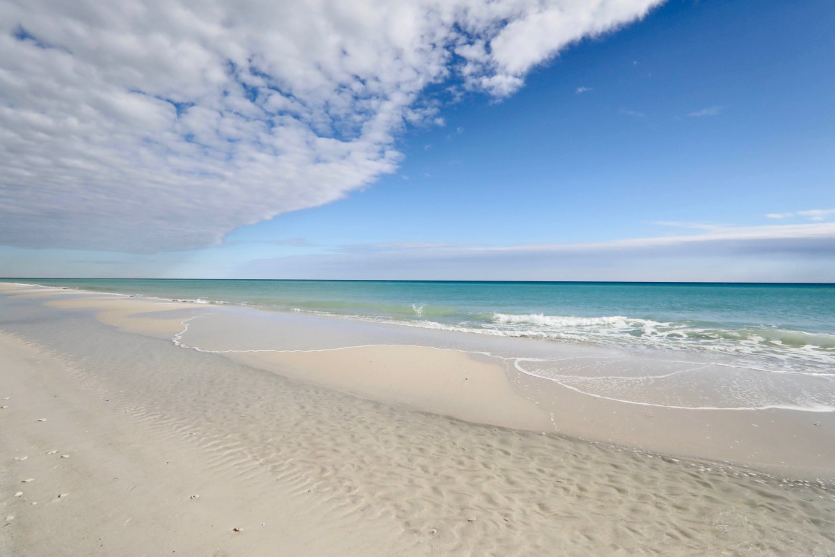 A serene beach scene with gentle waves lapping at the sandy shore under a partly cloudy sky.