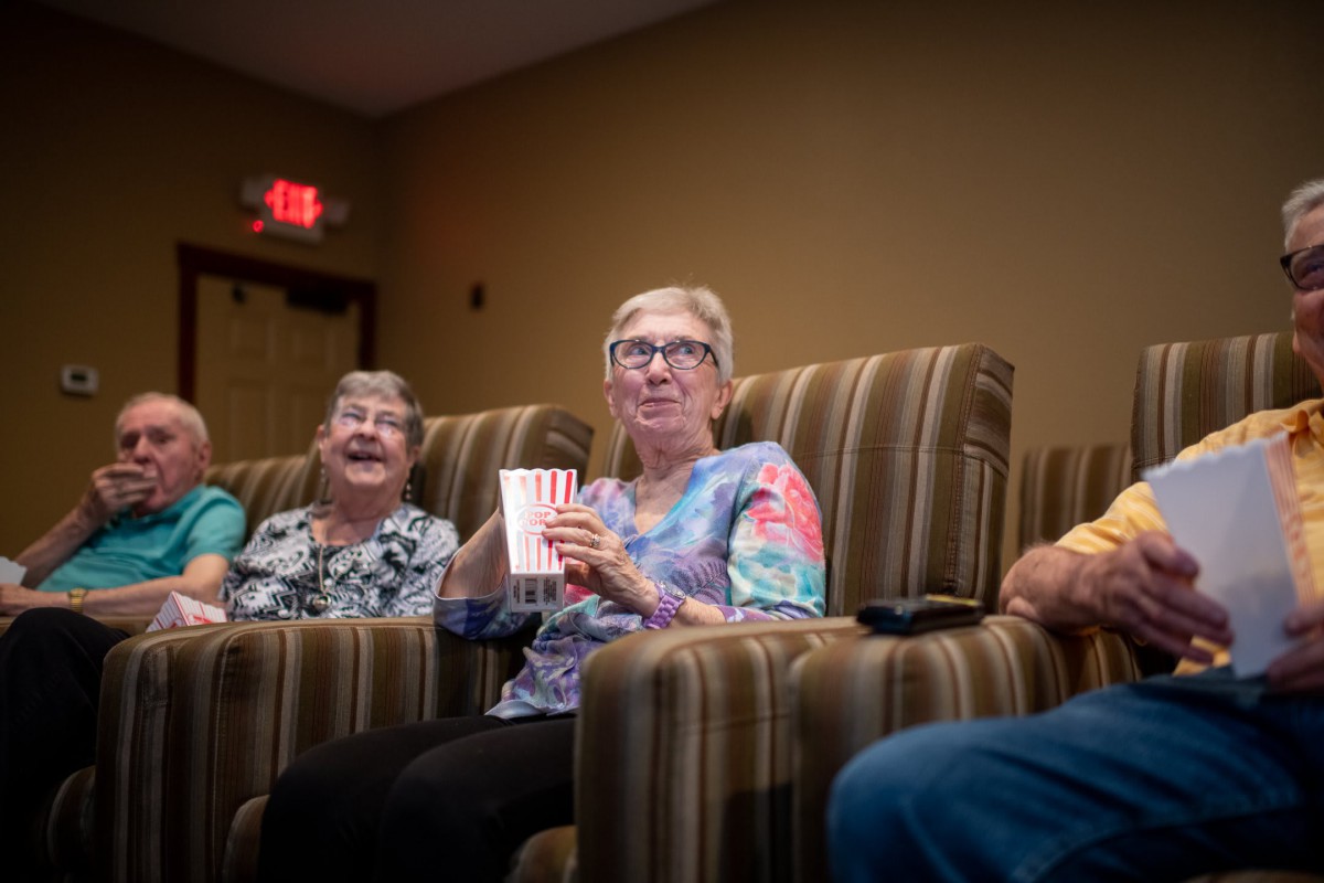 A group of seniors enjoying a movie in a theater, with one holding a box of popcorn.