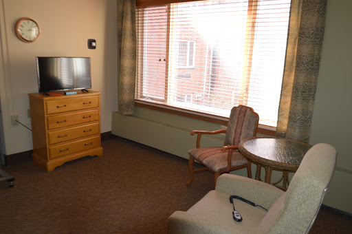 A cozy living room setup featuring a dresser, television, chair, and large window.