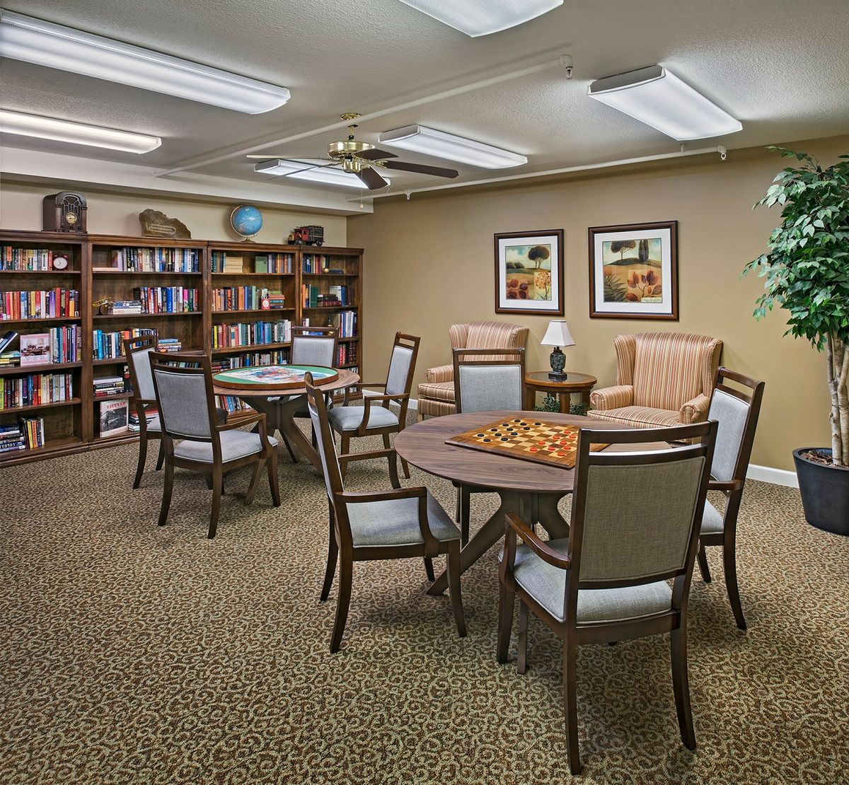 A cozy library room with multiple tables and chairs, surrounded by bookshelves and decorated with wall art.