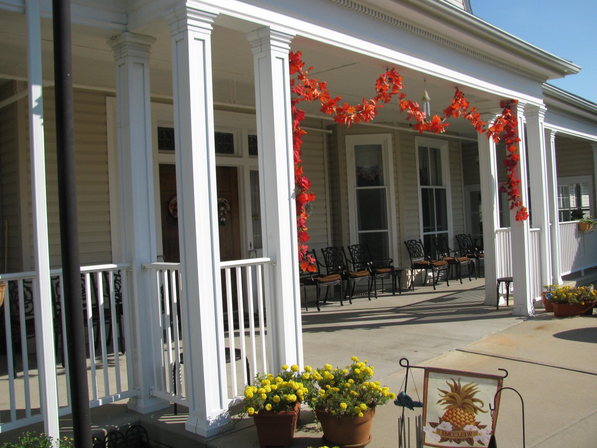 A porch decorated with autumn leaves, potted flowers, and seating area.