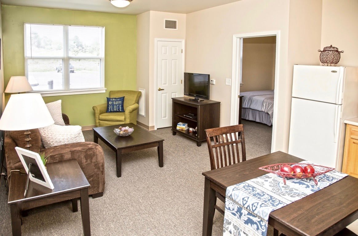 A cozy apartment living room with a television, coffee table, and dining area.