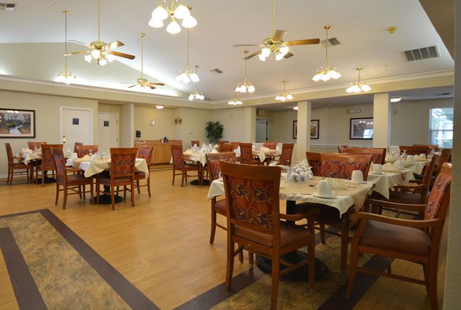 A spacious dining room with neatly arranged tables and chairs, illuminated by ceiling lights.