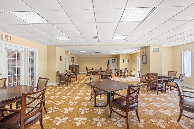 A spacious, well-lit dining room with multiple tables and chairs arranged on a patterned carpet.
